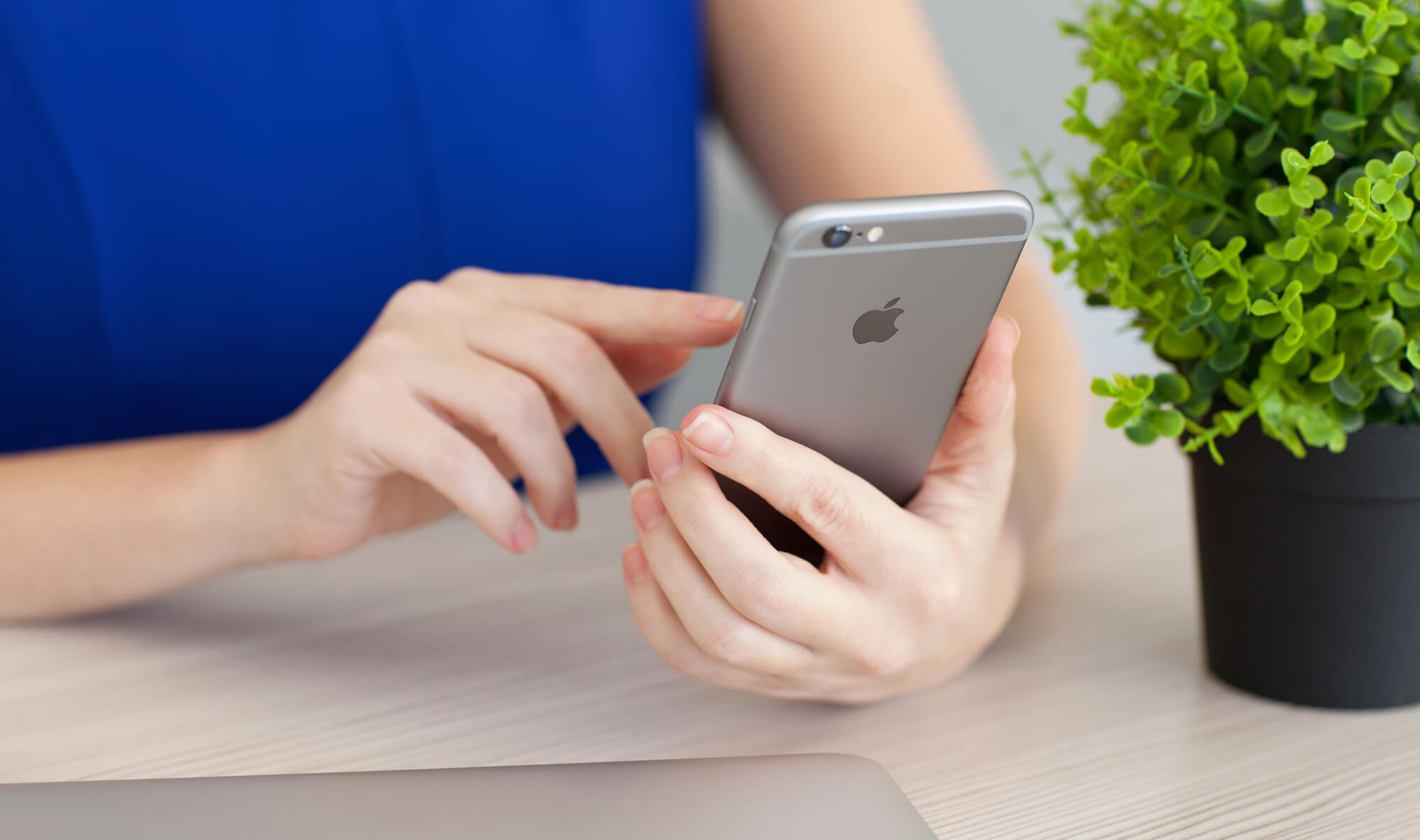 Image of woman placing thumb on phone next to laptop.